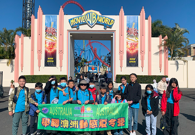 同學在澳洲華納電影世界(Movie World)門前拍攝團體照,背景可見過山車與主題建築 | 澳洲遊學團