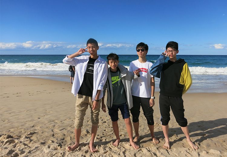 同學在沙灘上合影,赤腳踏在沙中,背景為碧海藍天,展現夏日戶外活動氛圍 | 澳洲遊學團