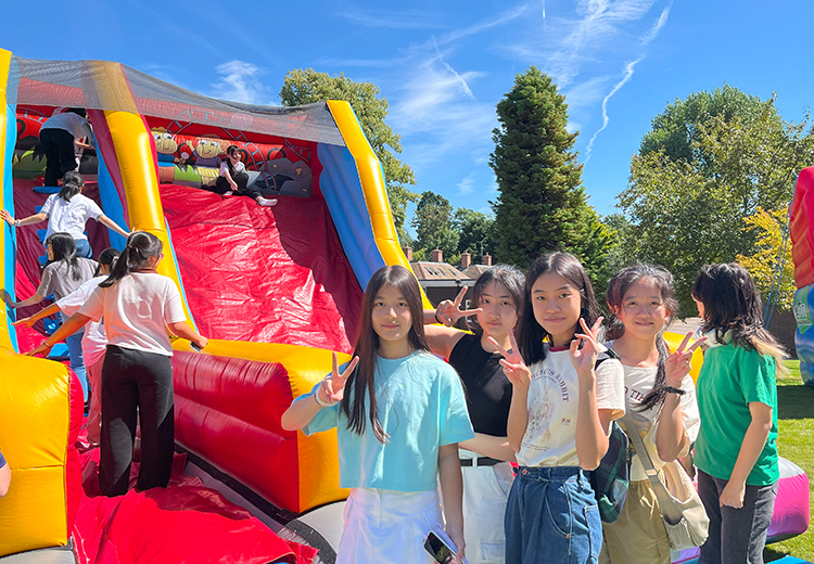 同學在陽光明媚的校園草地上,充氣滑梯旁合照,穿著輕便衣服,展現夏日活動的熱情與青春活力 | 英國遊學團